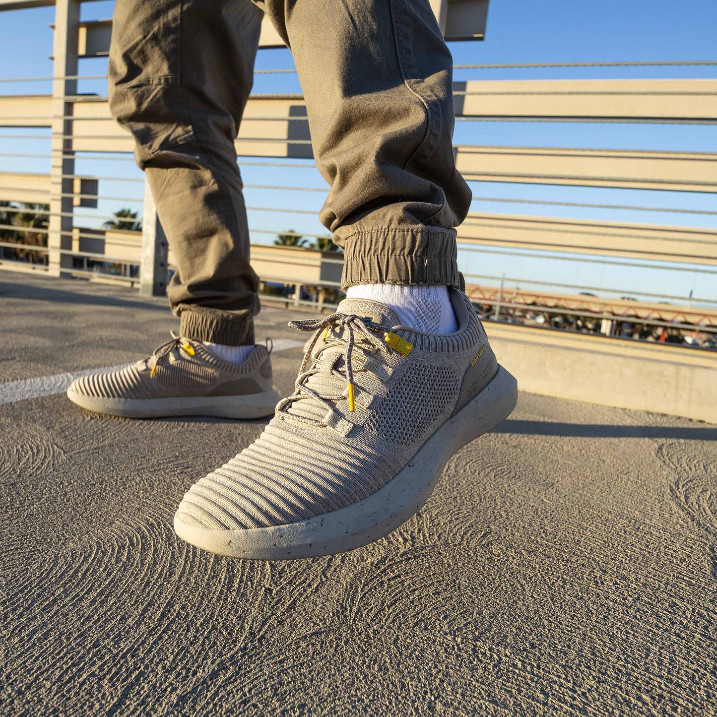 Lifestyle Image of a man wearing dark green cargo pants on the roof of a parking lot during golden hour wearing sand colored SNNCE Tan Sneakers